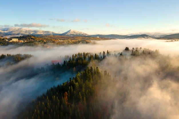 Luftaufnahme eines kleinen entfernten Dorfhauses auf einem Hügel in nebligen Herbstbergen bei Sonnenaufgang.