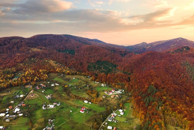 Luftaufnahme eines ländlichen Dorfes mit kleinen Häusern zwischen herbstlichen Berghügeln, die mit gelben und grünen Kiefern bedeckt sind