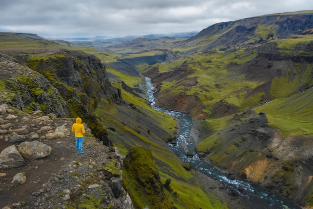 Luftaufnahme eines Mannes, der am Rand einer Klippe steht und das isländische Hochlandtal und den Haifoss-Wasserfall genießt