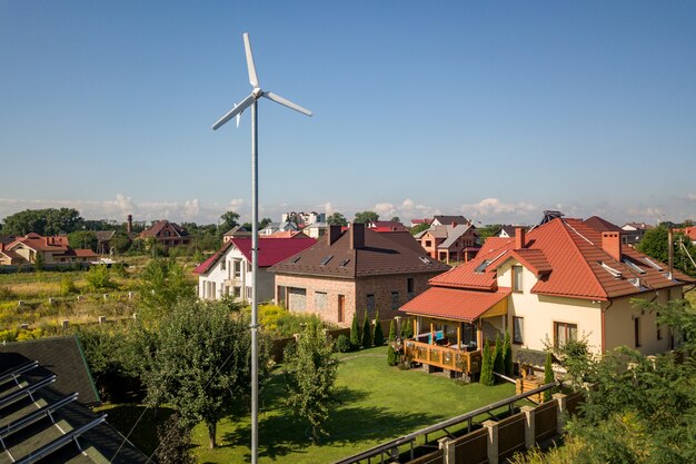 Luftaufnahme eines neuen autonomen Hauses mit Sonnenkollektoren, Warmwasserbereitern auf dem Dach und einer windbetriebenen Turbine auf einem grünen Hof.