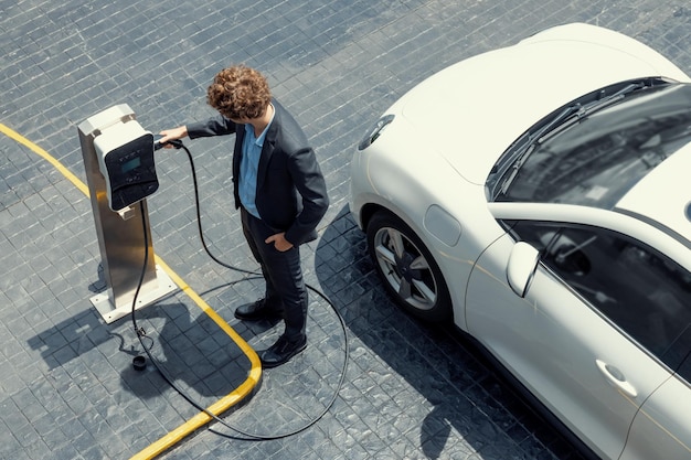 Luftaufnahme eines progressiven Geschäftsmannes mit EV-Auto, der die Batterie auflädt