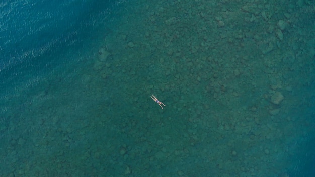 LUFTAUFNAHME: Frau, die auf Oberfläche des blauen Wassers schwimmt und schwimmt im transparenten Mittelmeer, Ansicht von oben nach unten, Sommerferienkonzept