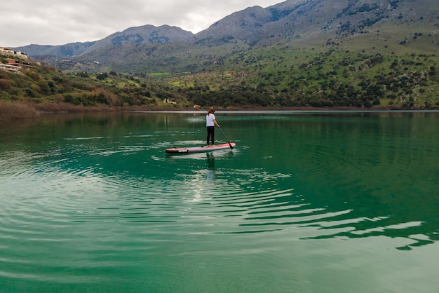 Luftaufnahme per Drohne einer Frau, die Stand Up Paddle oder SUP auf dem See praktiziert