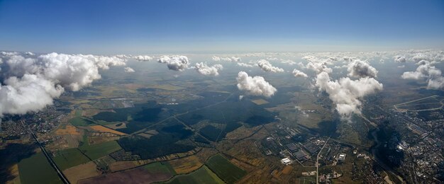 Luftaufnahme vom Flugzeugfenster in großer Höhe der entfernten Stadt, bedeckt mit weißen, geschwollenen Kumuluswolken.