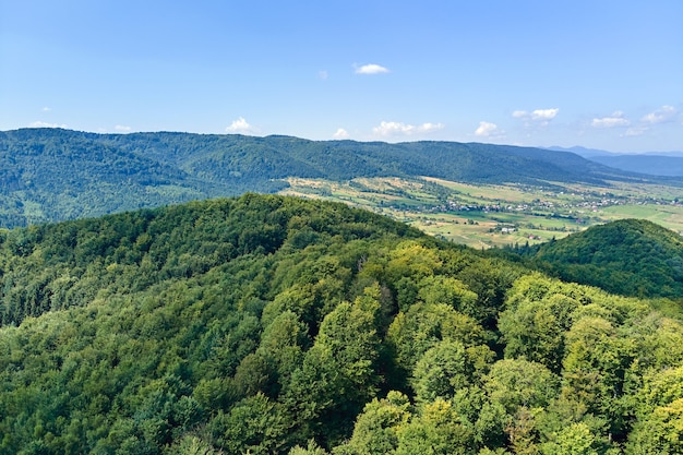 Luftaufnahme von Berghügeln, die an einem hellen Sommertag mit dichten grünen Wäldern bedeckt sind.