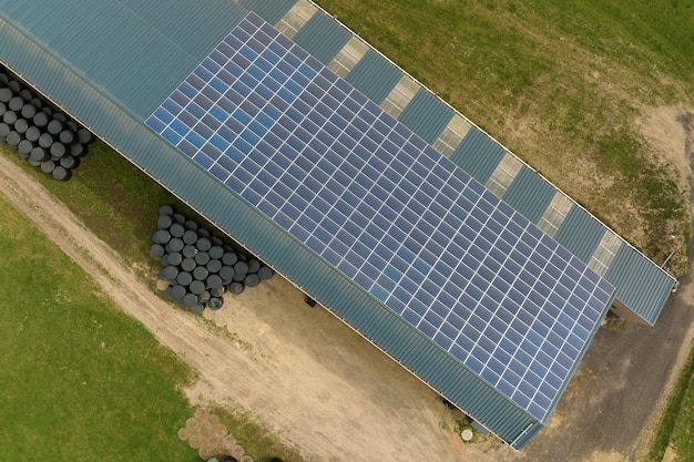 Luftaufnahme von blauen Photovoltaik-Solarmodulen, die auf dem Dach des landwirtschaftlichen Gebäudes montiert sind, um sauberen ökologischen Strom zu erzeugen Erzeugung von erneuerbarem Energiekonzept