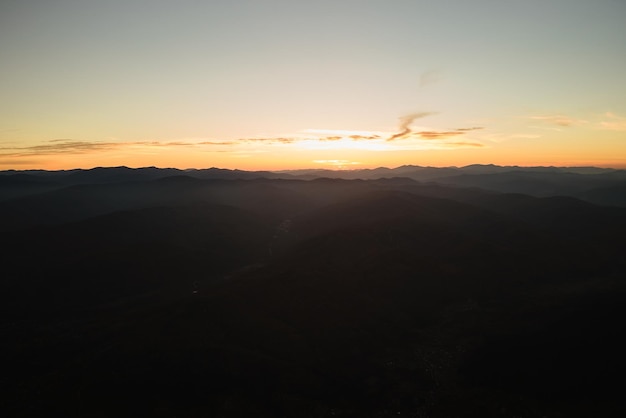 Luftaufnahme von dunklen Berghügeln bei Sonnenuntergang. Dunstige Gipfel und neblige Täler am Abend.