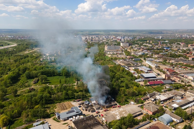 Luftaufnahme von Feuerwehrleuten, die ein zerstörtes Gebäude in Brand mit eingestürztem Dach und aufsteigendem dunklem Rauch löschen.