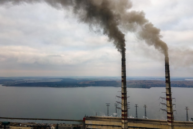 Luftaufnahme von hohen rohren des kohlekraftwerks mit schwarzem rauch, der die umweltverschmutzende atmosphäre nach oben bewegt.