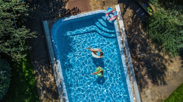 Luftaufnahme von Kindern im Schwimmbad von oben, glückliche Kinder schwimmen auf aufblasbaren Ringkrapfen und haben Spaß im Wasser während des Familienurlaubs im Resort