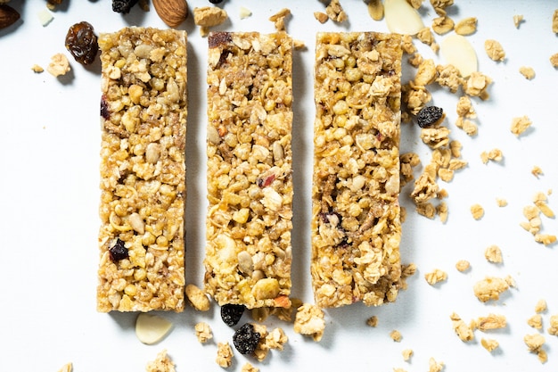 Luftaufnahme von Müsli- oder Müsliriegeln mit getrockneten Früchten und Rosinen auf einer weißen Oberfläche. Gesundes und natürliches Ernährungskonzept.