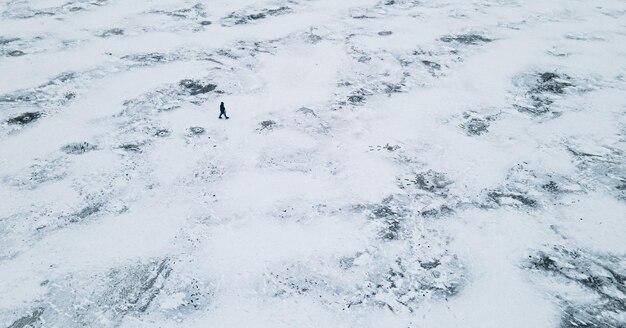 Luftaufnahme von oben auf eine Person geht im Winter zwischen einem eisigen See spazieren