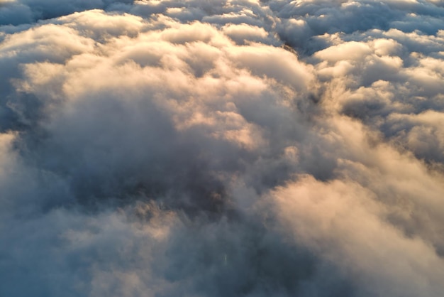 Luftaufnahme von oben in großer Höhe von dichten, geschwollenen Kumuluswolken, die abends fliegen. Erstaunlicher Sonnenuntergang aus Sicht des Flugzeugfensters