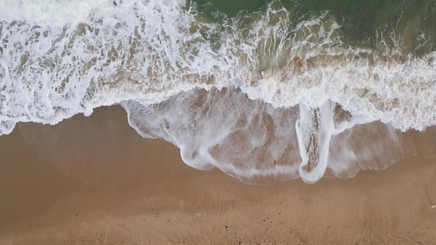 Luftaufnahme von oben nach unten an einem Sandstrand mit Zeitlupe der Meeresbrandung