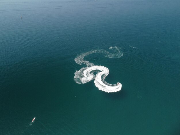 Luftaufnahme von oben nach unten der Wasserschaumspur mit schönem tiefblauem Schatten des Ozeans schöne weiße Spur auf