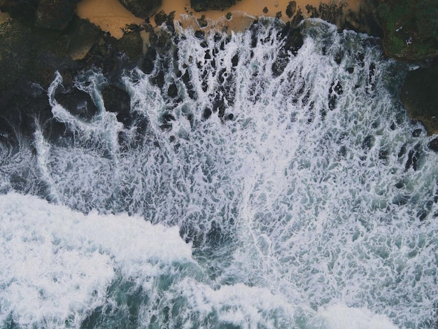 Luftaufnahme von oben nach unten von riesigen Meereswellen, die am Korallenstrand zusammenbrechen und schäumen