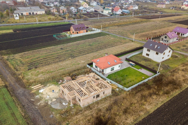 Luftaufnahme von oben nach unten von zwei Privathäusern, eines im Bau mit Holzdachrahmen und eines mit rotem Ziegeldach.