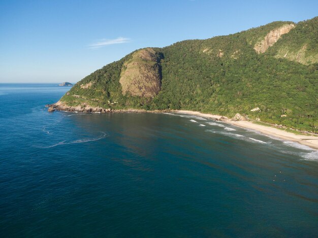 Luftaufnahme von Prainha Beach, einem Paradies auf der Westseite von Rio de Janeiro, Brasilien. Große Hügel herum. Sonniger Tag im Morgengrauen. Grünliches Meer. Drohnenfoto.