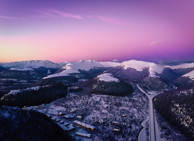 Luftaufnahme von schneebedeckten Bergstraßenhäusern und violettem Himmel