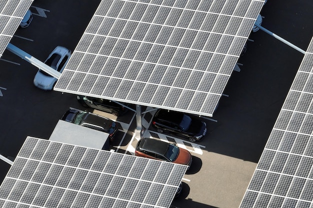 Luftaufnahme von Sonnenkollektoren, die als Schattendach über einem Parkplatz mit geparkten Autos installiert sind, um effektiv sauberen Strom zu erzeugen. In die städtische Infrastruktur integrierte Photovoltaik-Technologie