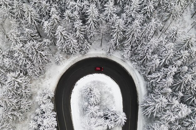 Luftbild auf der Straße im Wald mit einem Auto im Winter. Winterlandschaft mit hohen Kiefern bedeckt mit Schnee.