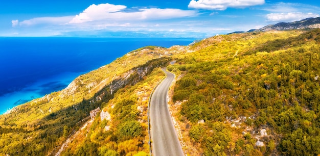 Luftbild der Bergstraße in der Nähe des blauen Meeres Waldhimmel mit Wolken bei Sonnenuntergang im Herbst Lefkada Griechenland Draufsicht der Straße Orangenbäume Hügel im Herbst Schöne Landschaft mit Autobahn und Küste