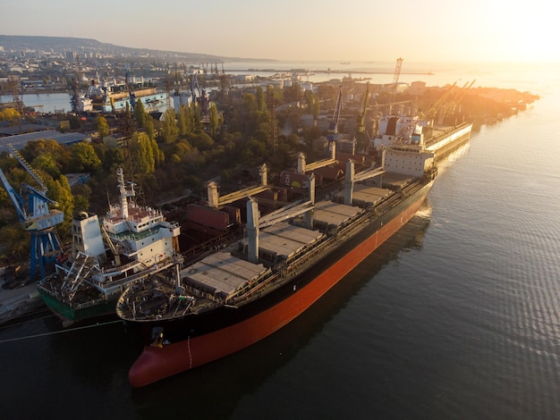 Luftbild des großen Frachtschiffs Massengutfrachter wird bei Sonnenuntergang mit Weizenkorn im Hafen beladen