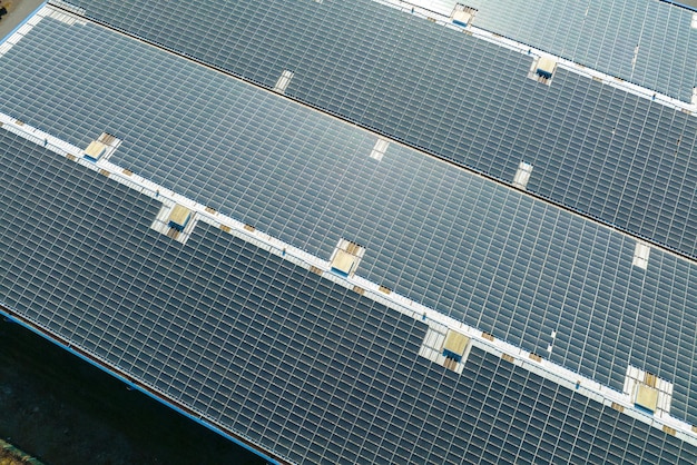 Luftbild des Solarkraftwerks mit blauen Photovoltaikmodulen, die auf dem Dach des Industriegebäudes zur Erzeugung von grünem Ökostrom montiert sind Produktion eines nachhaltigen Energiekonzepts