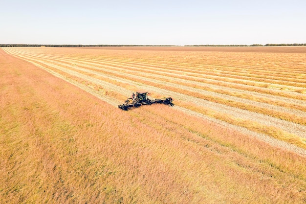 Luftbild-Drohne des Erntefeldes mit Traktor mäht trockenes Gras Herbstgelbes Feld mit einem Heuhaufen nach der Ernte von oben Ernten auf den Feldern Heu für den Winter auffüllen Ansicht von oben