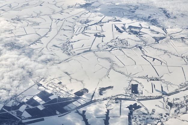 Luftbild über Wolken bis zu schneebedeckten Flüssen, Feldern und Straßen im Winter, frische, frostige Luft