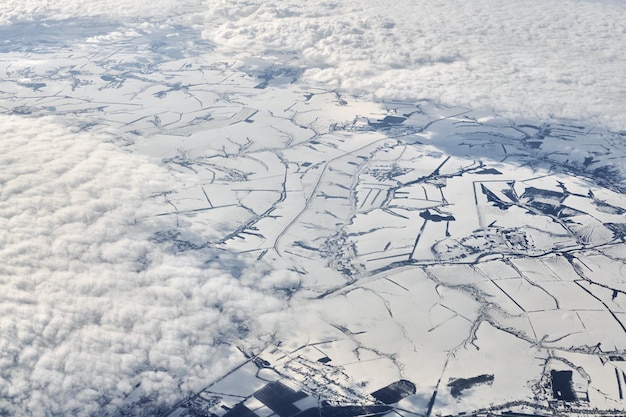 Luftbild über Wolken bis zu schneebedeckten Flüssen, Feldern und Straßen im Winter, frische, frostige Luft