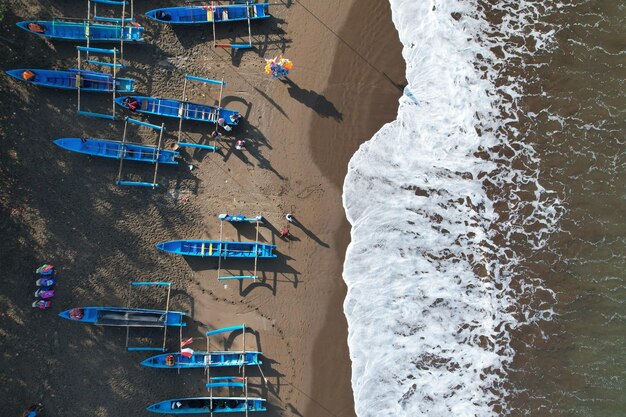 Luftbild von blauen Fischerbooten, die am schwarzen Sandstrand verankert sind. Tourismus. Meereslandschaft. Wellen.