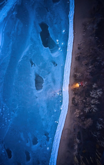 Luftbild von oben auf ein einsames Auto an der gefrorenen Meeresküste mit Scheinwerfern auf einer einsamen Straße
