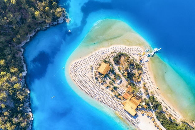 Luftbild von Sandstrand mit Sonnenschirmen grünen Bäumen Berg bei Sonnenuntergang im Sommer Blaue Lagune in Ölüdeniz Türkei Tropische Landschaft mit Meeresbucht Insel weißer Sandstrand blaues Wasser Draufsicht