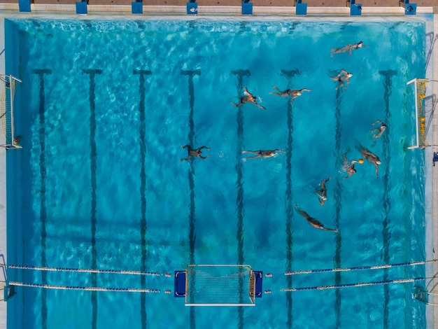 Luftdrohne Draufsichtaufnahme von Menschen, die im Wasserball im türkisfarbenen Wasserbecken konkurrieren