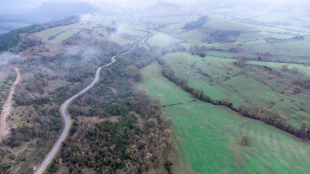 Luftdrohnenansicht der Bergstraße und der grünen Wiesen an bewölkten Tagen mit Nebel