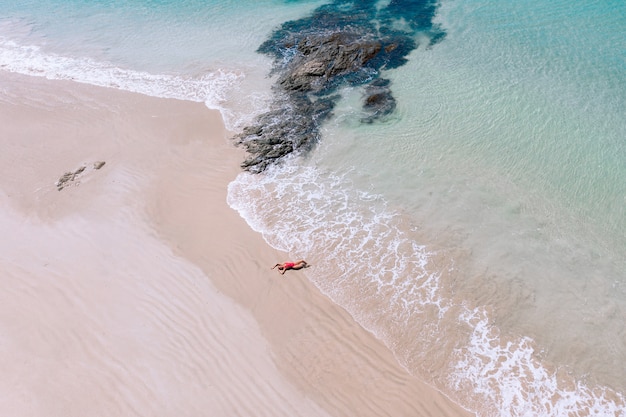 Luftdrohnenansicht der jungen Frau im roten Bikini sonnen sich am Strand mit weißem Sand