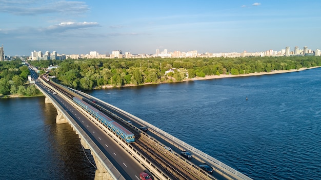 Luftdrohnenansicht der Metro-Eisenbahnbrücke mit Zug und Dnjepr von oben, Skyline der Stadt Kiew, Ukraine