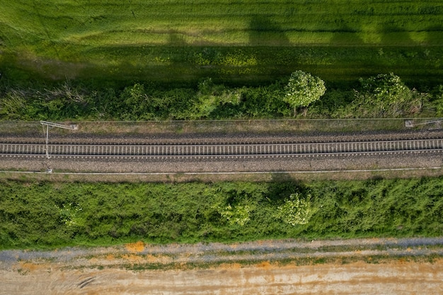 Luftdrohnenaufnahme einer Eisenbahnstrecke zwischen ländlichen Feldern und Vegetation