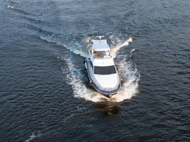 Luftdrohnenaufnahme einer kleinen motorisierten weißen Yacht, die auf dem Meer segelt