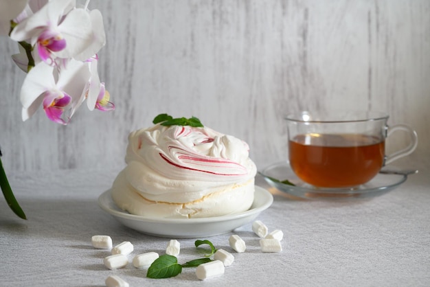 luftige Baisertorte auf hellem Hintergrund und eine Tasse Tee umrahmt von einer blühenden weißen Orchidee