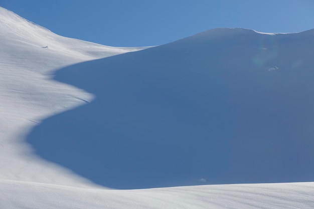Luftlandschaft aus weißem Schnee, die ein grafisches Texturspiel aus Licht und Schatten bildet