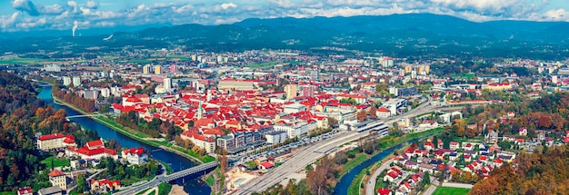 Luftpanoramablick im Herbst auf die Stadt Celje in Slowenien. Herbstbäume, grüne Wiesen und rote Dächer. Reisehintergrund im Freien.