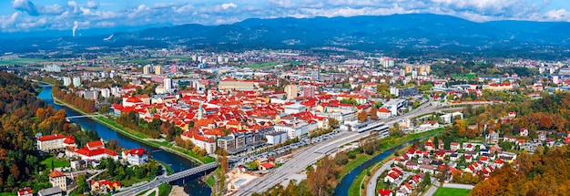 Luftpanoramablick im Herbst auf die Stadt Celje in Slowenien. Herbstliche Bäume, grüne Wiesen und rote Dächer. Reisehintergrund im Freien.