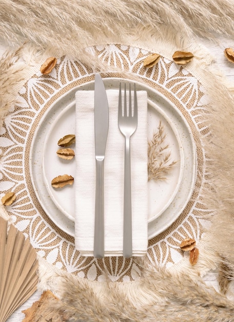 Lugar de mesa de casamento com garfo e faca sobre um guardanapo na vista superior de placemat boêmio. Cena Boho Tropical com plantas secas, folhas de palmeira e capim-dos-pampas, camada plana