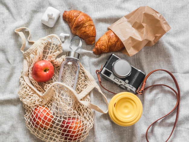 Lugar de piquenique de verão croissants câmera de frutas café em um copo térmico em uma vista superior do cobertor cinza