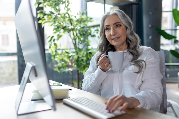 Lugar de trabalho Mulher de negócios bonita sentada ao computador e tomando chá