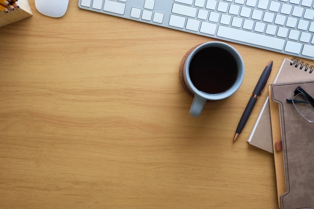Lugar de trabalho simples com teclado óculos caderno e xícara de café em mesa de madeira vista superior com espaço para o seu texto