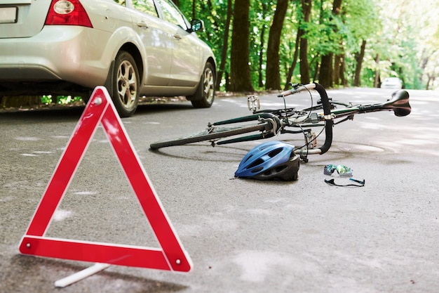 Lugar del desastre. Bicicleta y accidente de coche de color plateado en la carretera en el bosque durante el día