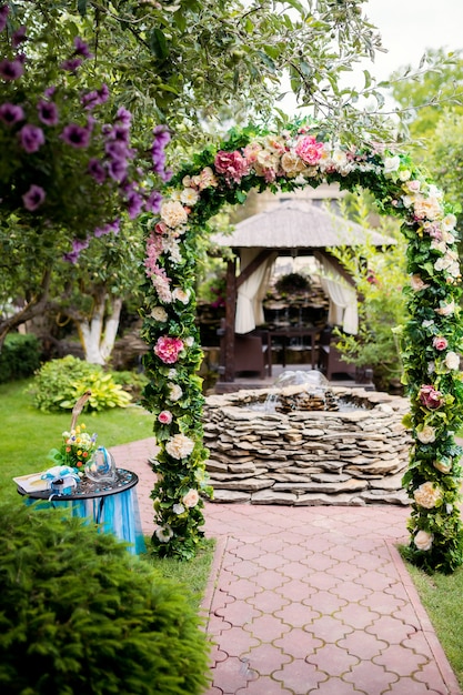 Lugar romántico con arco floral y fuente de piedras en el jardín.